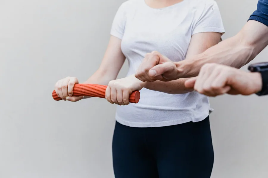 Eine Therapeutin führt die Hände einer Patientin, die eine Übungsrolle hält.