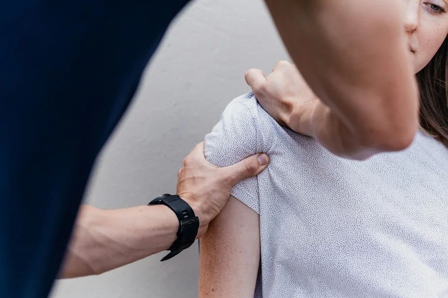 Eine Physiotherapeutin hält Schulter und Oberarm einer Patientin und prüft die Beweglichkeit.
